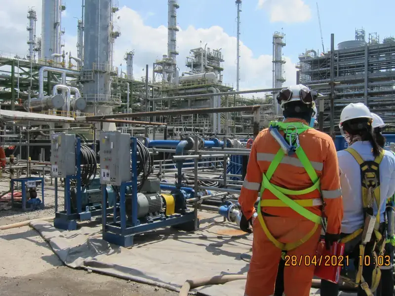CHC Chemical personnel in fall-protection harnesses beside a chemical circulation pump skid at a process plant