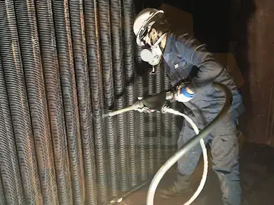 Technician in protective equipment cleaning a finned tube bank with dry ice